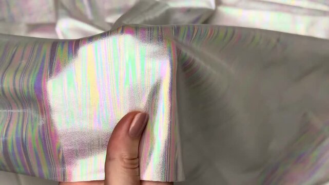 Silver stretch knit textile displaying an intense iridescent holographic effect with vertical rainbow reflections featuring an elastic texture suitable for unique fashion apparel projects.
