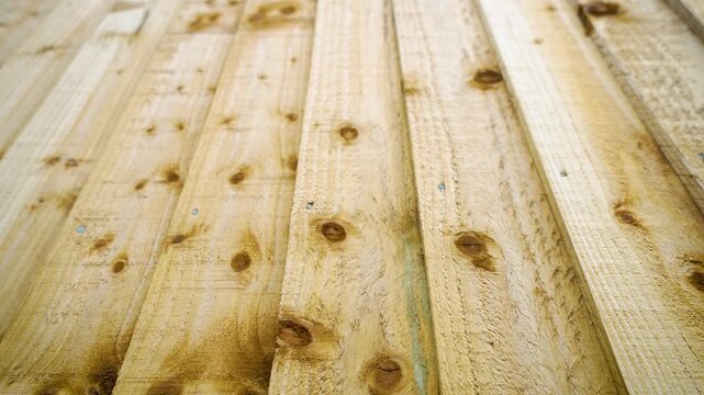Wood plank fence showcasing natural timber surface with knots and fasteners. Residential outdoor structure providing privacy separation and garden enclosure function. Wooden background texture