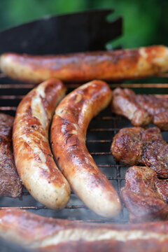 Zubereitung von Bratwurst und Schweinefleisch auf einem Holzkohlegrill.