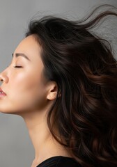 Fototapeta premium Beautiful Asian Woman with Long Wavy Hair Blowing in the Wind Profile View Serene Expression Beauty Concept