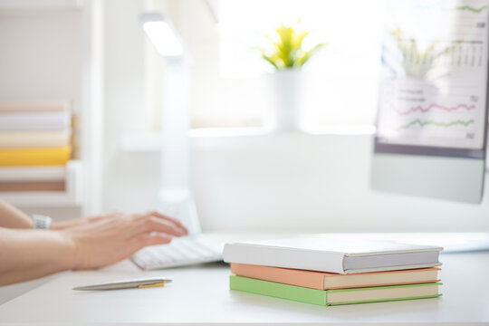 Books on table over blurred background of hands typing on computer keyboard in modern office workplace