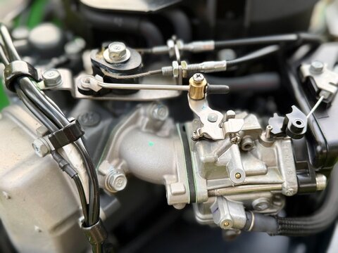 A close-up of a mechanic's hand adjusting a small carburetor linkage on a boat's outboard motor engine. A detailed shot showcasing mechanical repair, maintenance, and small engine troubleshooting.