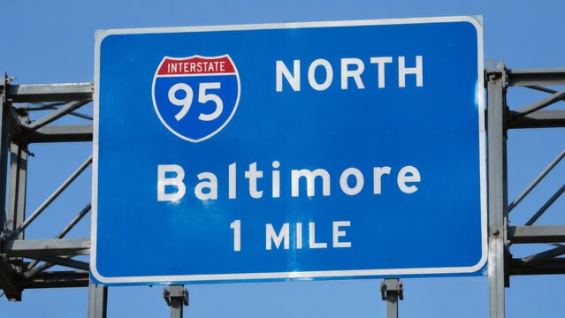 A large blue Interstate 95 highway sign directing traffic to Baltimore, mounted on a steel structure under a clear blue sky