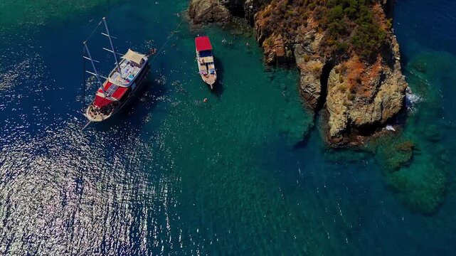 Aerial view of tour boats anchored in clear turquoise water with people swimming near a rocky coast, ideal for summer travel, tourism, vacation, cruise and Mediterranean lifestyle content.