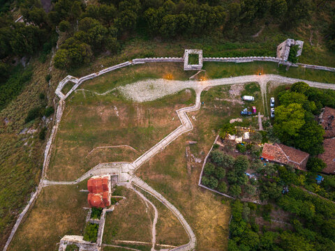 Aerial view of Berat Castle featuring the historic stone walls, the red-domed Holy Trinity Church, and winding paths surrounded by lush greenery in Berat, Qarku i Beratit, Albania.