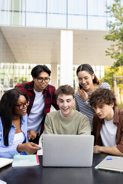 University students collaborating on a project using laptop outdoors
