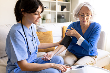 Obraz premium Nurse measuring blood pressure of senior woman at home