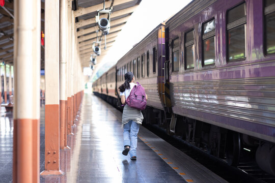 Woman traveler carrying a backpack running alongside a moving train on a station platform, highlighting concepts of travel, urgency, and transportation.