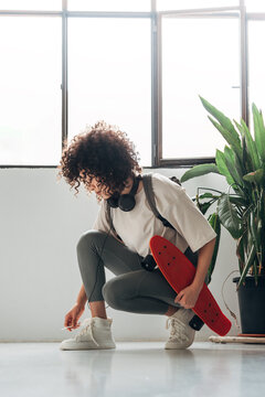 Woman tying shoelaces holding skateboard ready to skate