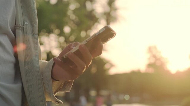 Close-up of men's hands with a mobile in their hands typing sms.  Hands using mobile over sunset.  Person is typing a text message on a cell phone phone - close-up. 