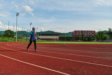 Fototapeta premium Young Woman Running on Outdoor Track Wearing Hijab and Sportswear for Fitness and Training