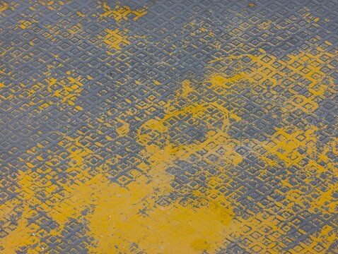 Close-up of worn yellow paint over a patterned gray metal surface, creating an industrial grunge texture ideal for backgrounds, design projects, and urban themes.