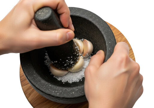 Hands crushing garlic cloves with coarse salt in a stone mortar and pestle isolated on transparent background