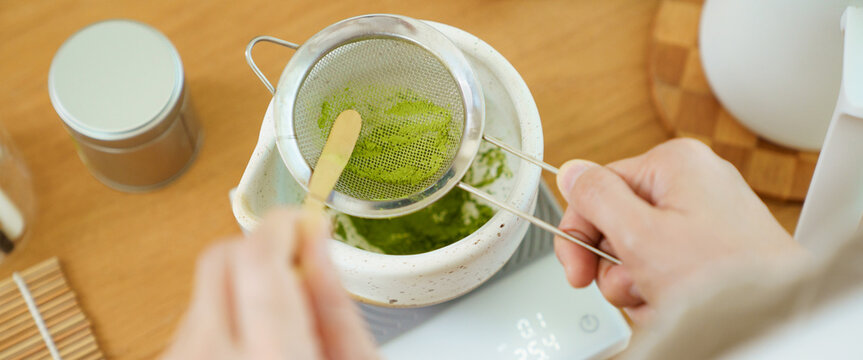 Person sifting vibrant green matcha powder during a tea preparation session