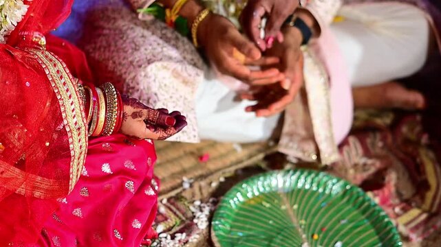 Close-up footage of bride and groom hands participating in traditional Hindu wedding rituals during a marriage ceremony in India. The scene captures sacred customs, ceremonial offerings