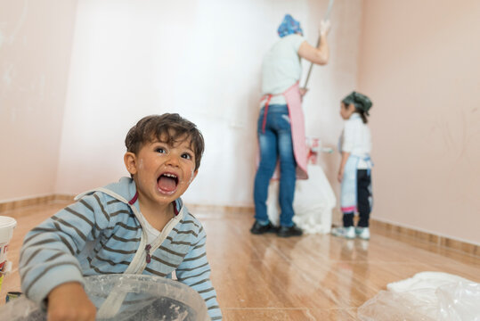 Mother and her children painting home room. Funny boy dirty looking at camera