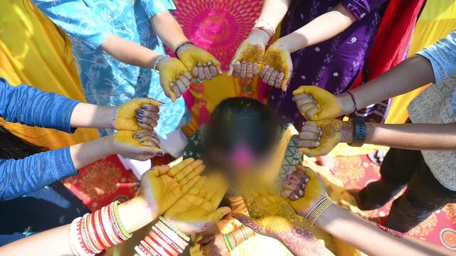 Close-up footage of a traditional Indian Haldi ceremony where family members and friends apply turmeric paste to the bride before marriage. The pre-wedding ritual symbolizes purification, blessings.