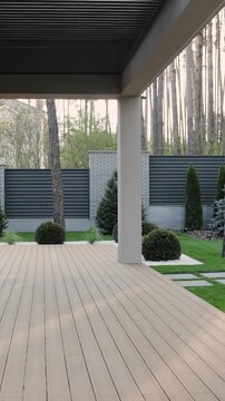 Vertical video. Wooden terrace with lattice roof near modern house and landscaped garden at sunset.