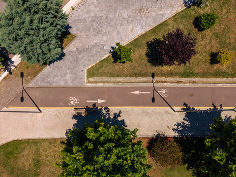 Aerial view of a two-way bicycle lane with white directional arrows and bike symbols passing through a green park with paved walkways and trees in Gradishte, Fier County, Albania.