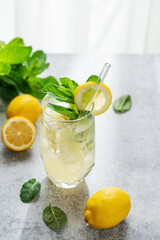 Fototapeta premium A summer drink with lemon, mint, and ice in a two glasses against a sunny window background.