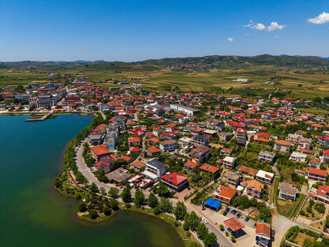 Aerial view of the town of Gradishte with red-roofed houses along the lake shore and green fields under a clear blue sky Gradishte, Fier County, Albania.