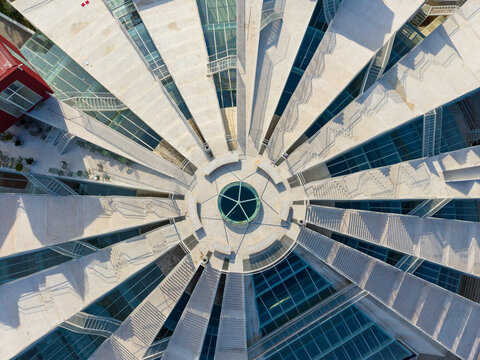 Aerial view of the Pyramid of Tirana featuring its radial concrete structure, outdoor stairs, and glass panels under bright daylight in Tirane, Tirana County, Albania.