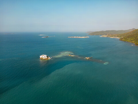 Aerial view of a secluded white building on a small rocky island surrounded by turquoise Caribbean waters and distant lush hills in Guanaja, Bay Islands Department, Honduras.
