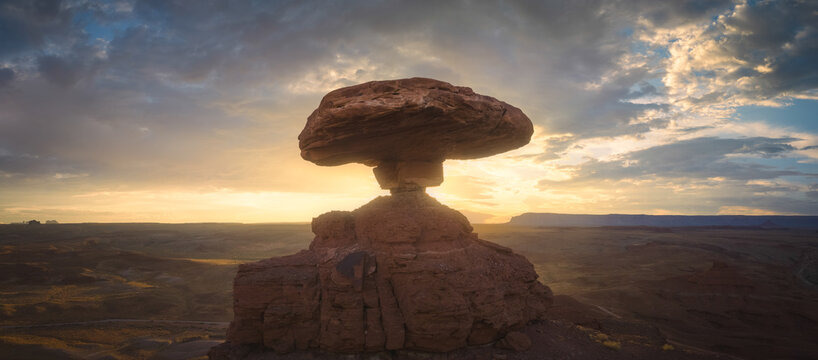 Aerial view of the Mexican Hat rock formation at sunset with dramatic clouds over the desert landscape in Mexican Hat, Utah, United States.
