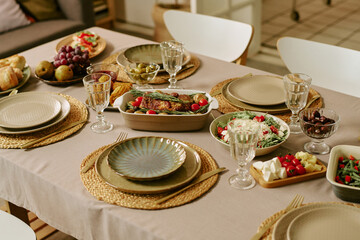 Fototapeta premium No people closeup of family table setting displaying Sunday lunch with plated meal, salad, bread, fruit, serving dishes. Supporting family dining, weekend gathering, home lifestyle marketing