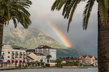 Large palm trees on a wet promenade framing a vibrant rainbow over the sea and mountains in Tivat. Montenegro 24.04.2026 © Dragan