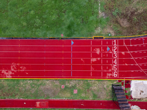 Aerial view of a red athletics running track with white lane markings and numbered starting positions next to a green field Merida, Yucatan, Mexico.