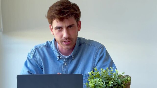 Confident young male professional speaking directly to the camera during a virtual meeting, actively gesturing and explaining concepts from his modern home office workspace