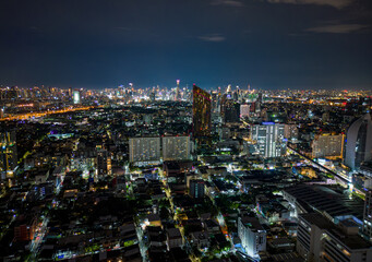 Naklejka premium Aerial night view of Bangkok skyline with illuminated skyscrapers, city lights, and modern urban architecture stretching across the Thai capital.