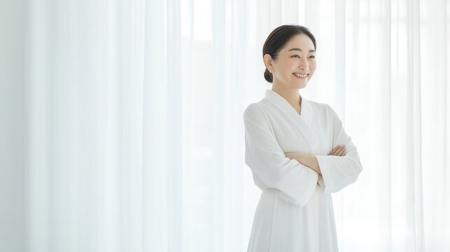 Lifestyle portrait of vibrant beautiful Japanese woman in her 50s, confident smiling pose with crossed hands, elegant casual outfit, bright airy white room, natural and studio soft lighting, clean col
