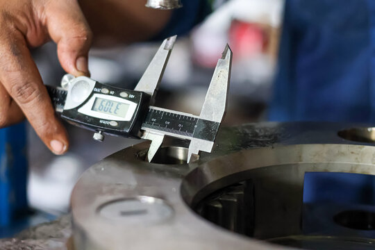 A technician uses a digital vernier caliper to measure the internal diameter of a hole on a heavy metal planetary carrier component.