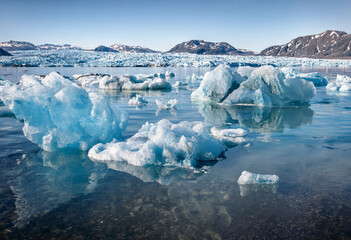 Blue icebergs floating in a calm glacial lake with snow-covered mountains in the background, under a clear, sky in a, cold arctic environment © come