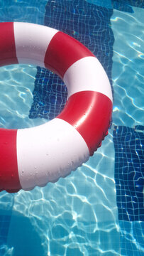 Summer vacation, summertime, leisure time, travel, tourism  concept. A classic red and white striped inflatable swim ring floats on the clear blue water of a tiled swimming pool. Space for text. 