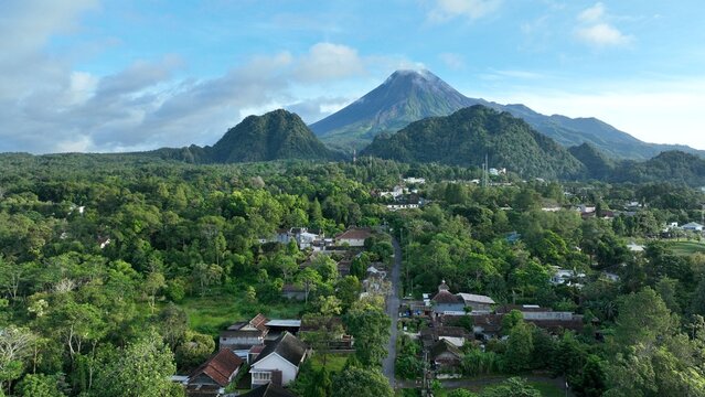 Aerial view of Kaliurang village nestled in lush tropical forest with Mount Merapi volcano in the background in Pakem, Special Region of Yogyakarta, Indonesia.