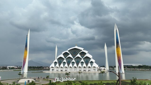 Aerial view of the modern Masjid Raya Al Jabbar with its unique geometric dome and tall minarets under a cloudy sky in Kecamatan Gedebage, Jawa Barat, Indonesia.