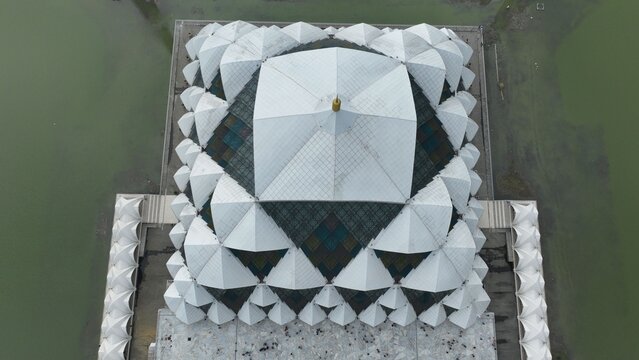 Aerial view of Masjid Raya Al Jabbar featuring its unique geometric white roof architecture and surrounding water in Kecamatan Gedebage, Jawa Barat, Indonesia.