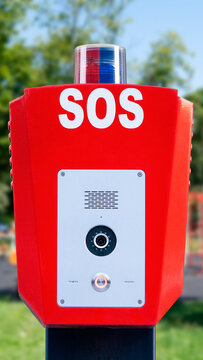 Emergency call box stands in a park near a playground during sunny day
