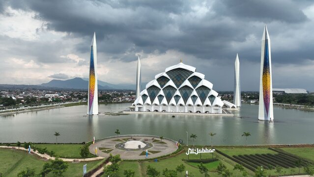 Aerial view of Masjid Raya Al Jabbar with its unique geometric architecture and tall minarets surrounded by water under a cloudy sky in Kecamatan Gedebage, Jawa Barat, Indonesia.