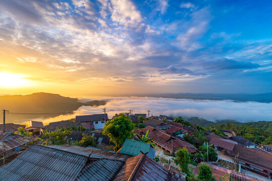 Stunning sunrise over Akha Pa Kluay mountain village in Doi Tung, Chiang Rai, Thailand, featuring a majestic sea of fog covering the valley under a golden morning sky.
