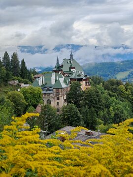 Historic S&uuml;dbahnhotel in Semmering Austria with its iconic deep green roof towers surrounded by lush forest and mountains under a cloudy sky in summer