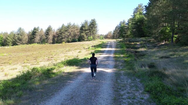 Aerial drone footage of a woman running through a heathland with forest