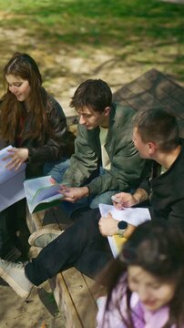 Three young students collaborate outdoors, discussing their studies. They work together on learning materials in a park setting.