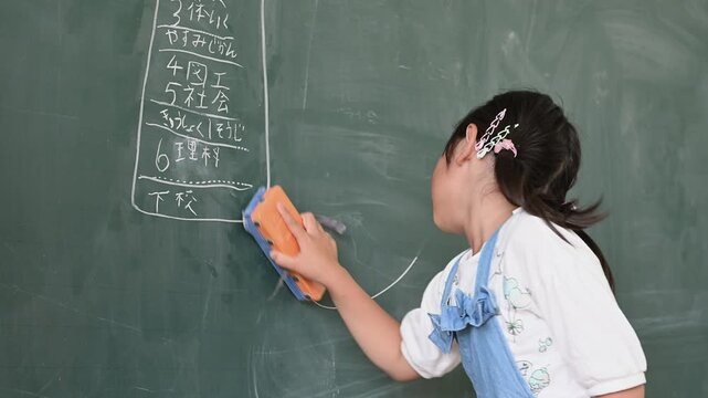 教室で笑顔で黒板を消す低学年の女子小学生	
