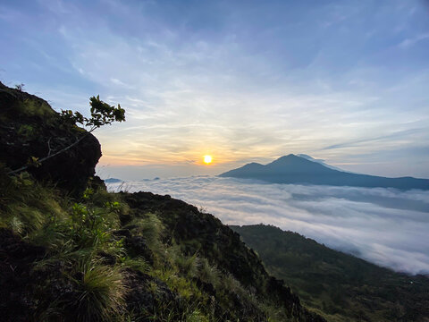 Trunyan and Abang Hills seen afar from Mount Batur in Kintamani, Bali, during golden sunrise with blue sky and scattered clouds in the morning. Concept of mountain hiking, adventure, and tourism