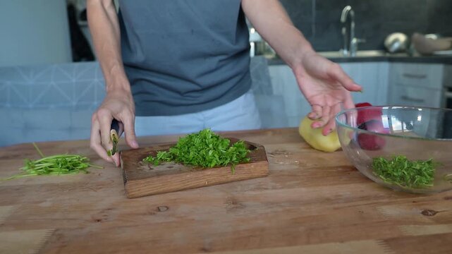 Person chopping fresh parsley and adding herbs into glass salad bowl video Full HD