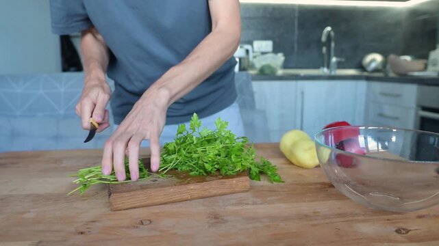 Person trimming fresh parsley stems on wooden cutting board in modern kitchen video Full HD